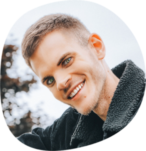 Fabian lächelt mit schräg gelegtem Kopf. Er hat helle Augen, kurze blonde Haare und eine dunkle Jacke mit flauschigem Kragen.