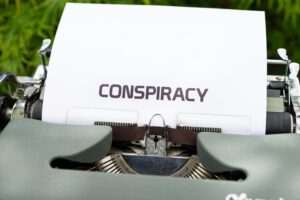 Eine Schreibmaschine mit einem weißen Blatt, auf dem Conspiracy (engl: Verschwörung) steht