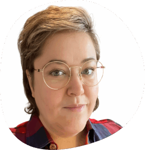 Sarah trägt eine runde. Brille, kurze blonde Haare und ein rot-blau kariertes Hemd