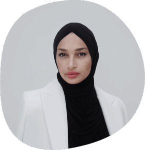 Meriem trägt eine schwarze Kopfbedeckung, einen schwarzen Rollkragenpullover und einen weißen Blazer