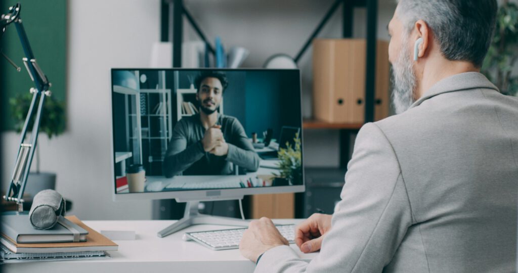 Ein Mann sitzt an einem Schreibtisch vor einem Computer. Er ist im Videocall mit einer anderen Person.