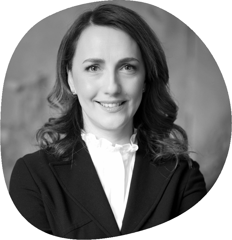 Natalia trägt schulterlange lockige Haare, ein weißes Hemd und einen schwarzen Blazer.