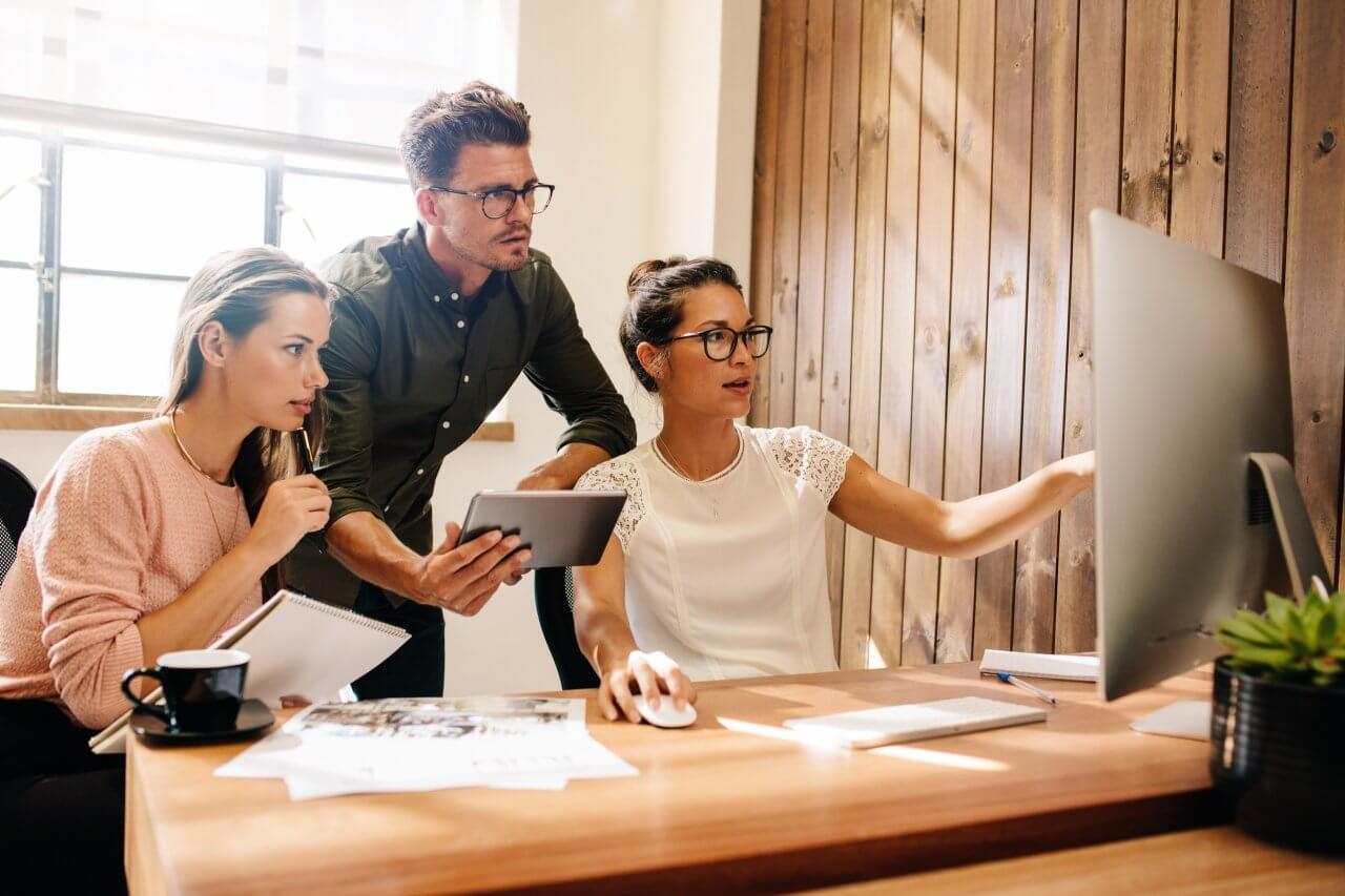 Drei Personen besprechen etwas an einem Bildschirm, Symbolbild für die kollaborative Stimmung, die unsere Trainings & Keynotes erzeugen.