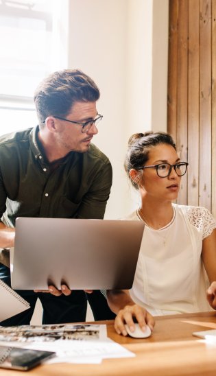 Drei Personen schauen gemeinsam auf einen Laptop und einen Monitor
