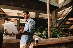 Mann steht mit einem Laptop in der Hand und arbeitet