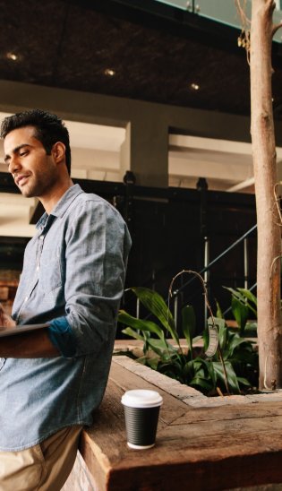Mann steht mit einem Laptop in der Hand und arbeitet