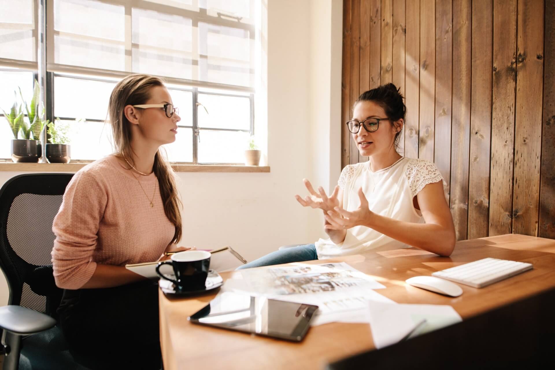 Zwei Frauen im Gespräch an einem Tisch im Sonnenlicht