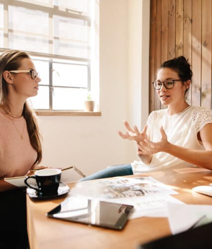 Zwei Frauen im Gespräch an einem Tisch im Sonnenlicht