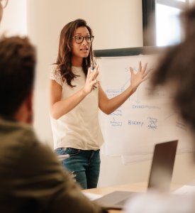 Frau erklärt etwas am Whiteboard vor sitzendem Publikum