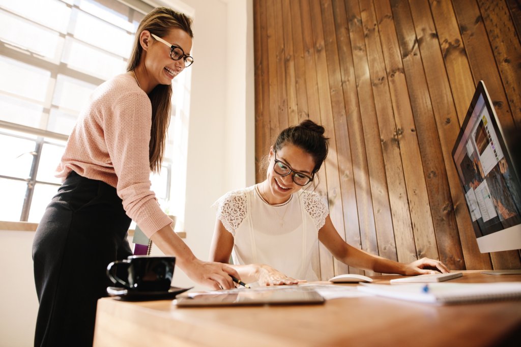Zwei Frauen arbeiten lachend gemeinsam am Schreibtisch