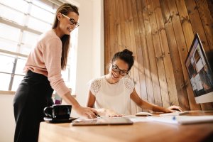 Zwei Frauen arbeiten lachend gemeinsam am Schreibtisch
