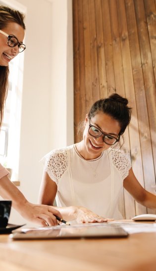 Zwei Frauen arbeiten lachend gemeinsam am Schreibtisch