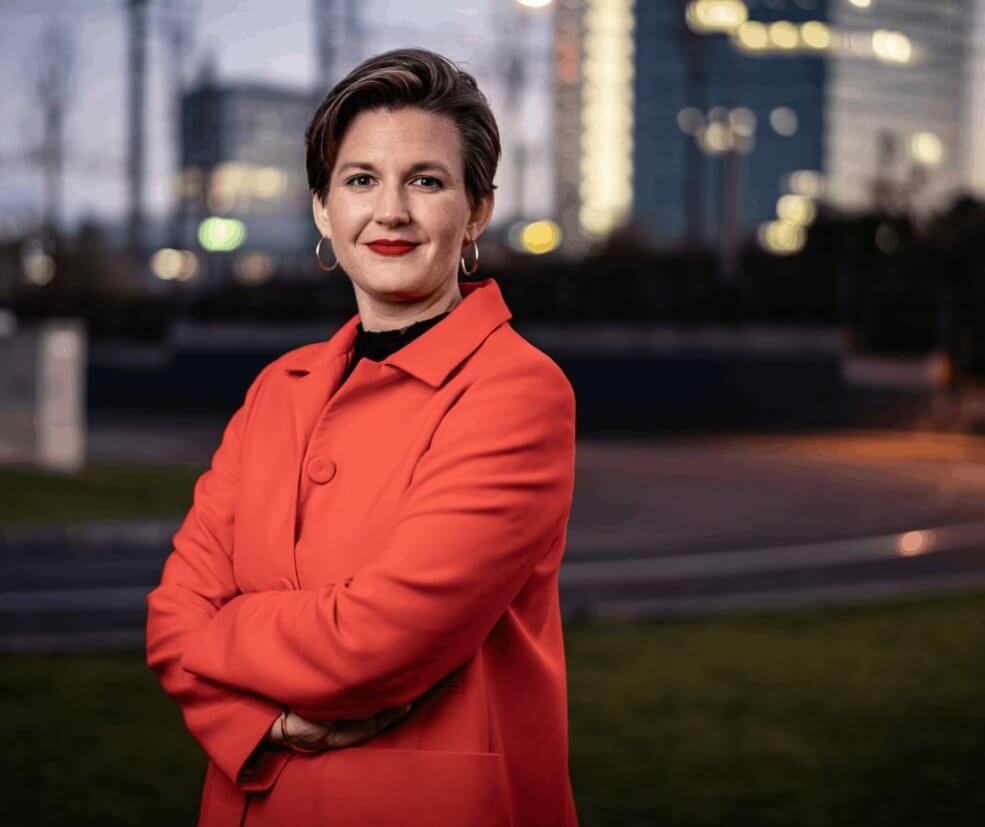 Dr. Simone Burel im roten Mantel vor abendlicher Stadtkulisse